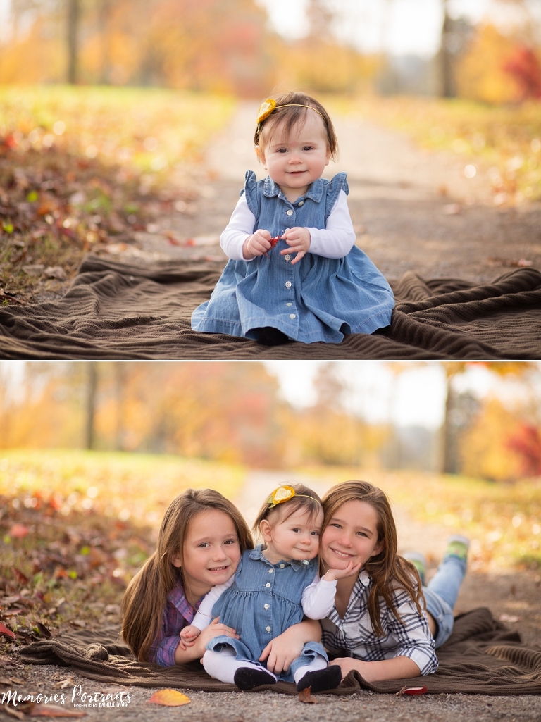 6 month old baby girl sitting on brown blanket while fall leaves fall around her and her sisters