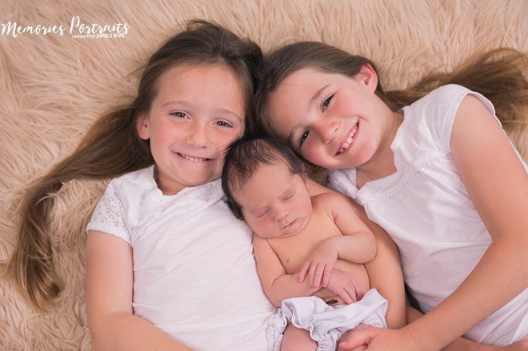 newborn posed on furry rug with two older sisters